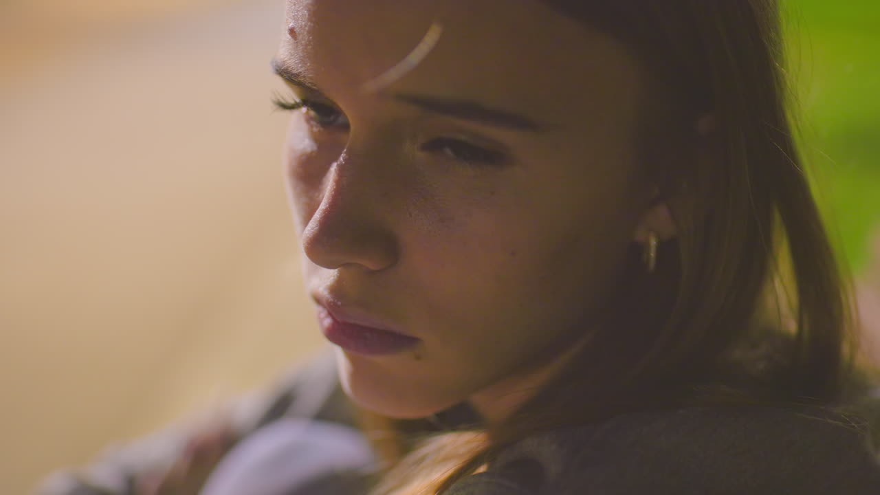 primer plano de una mujer al aire libre por la noche con una expresión cansada y somnolienta bajo una iluminación suave, el fondo sereno con vegetación borrosa y sombras sutiles se suma al estado de ánimo contemplativo