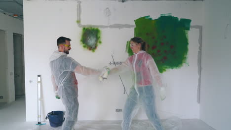 joyful guy and girl fight with spray paints and kiss in room