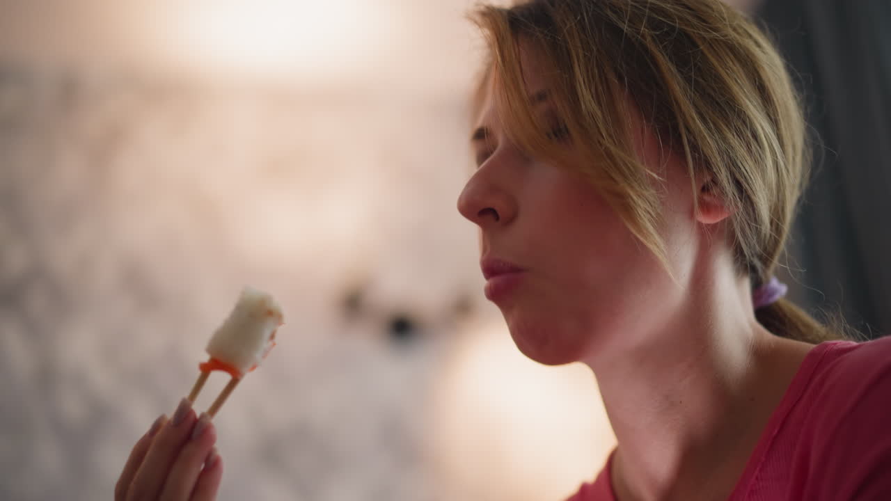 Young CEO on vacation eating sushi with chopstick inside hotel room featuring soft blurred background warm indoor light and relaxed expression
