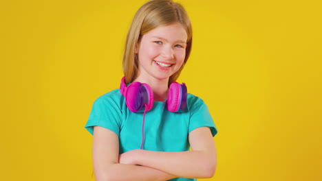 studio portrait of girl wearing headphones and smiling at camera against yellow background