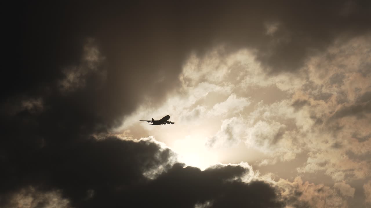 Silhouette of a plane flies through the clouds as the sun begins to set