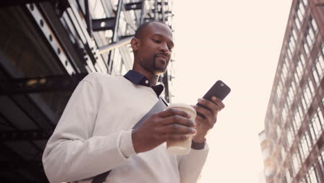 African-American-businessman-walking-through-city-using-smart-phone