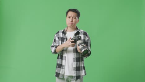 화가 난 아시아인 사진작가는 카메라에서 사진을 보고 스튜디오에서 녹색 스크린 배경에 서서 누군가에게 소리를 질렀다.