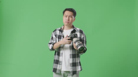 angry asian photographer looking at the pictures in the camera then shouting to someone while standing on green screen background in the studio