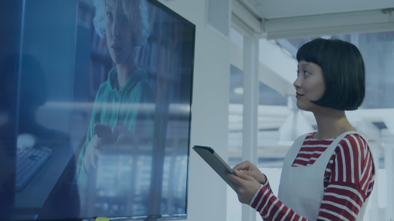 Animation of bar graph over asian woman looking at television and using digital tablet in office