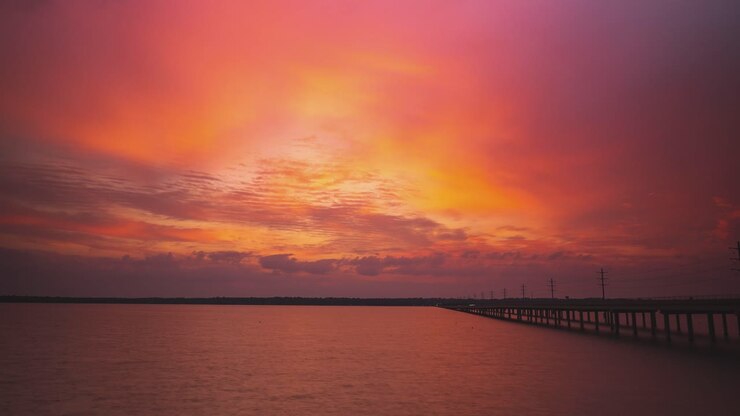 Epic cloudscape of brilliant orange red hues at sunset over river by highway bridge