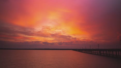 paisaje nuboso épico de brillantes tonos rojos naranja al atardecer sobre el río por el puente de la carretera
