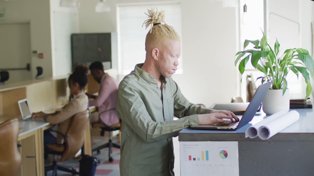 Portræt af glad albino afroamerikansk forretningsmand, der bruger bærbar computer på kreativt kontor