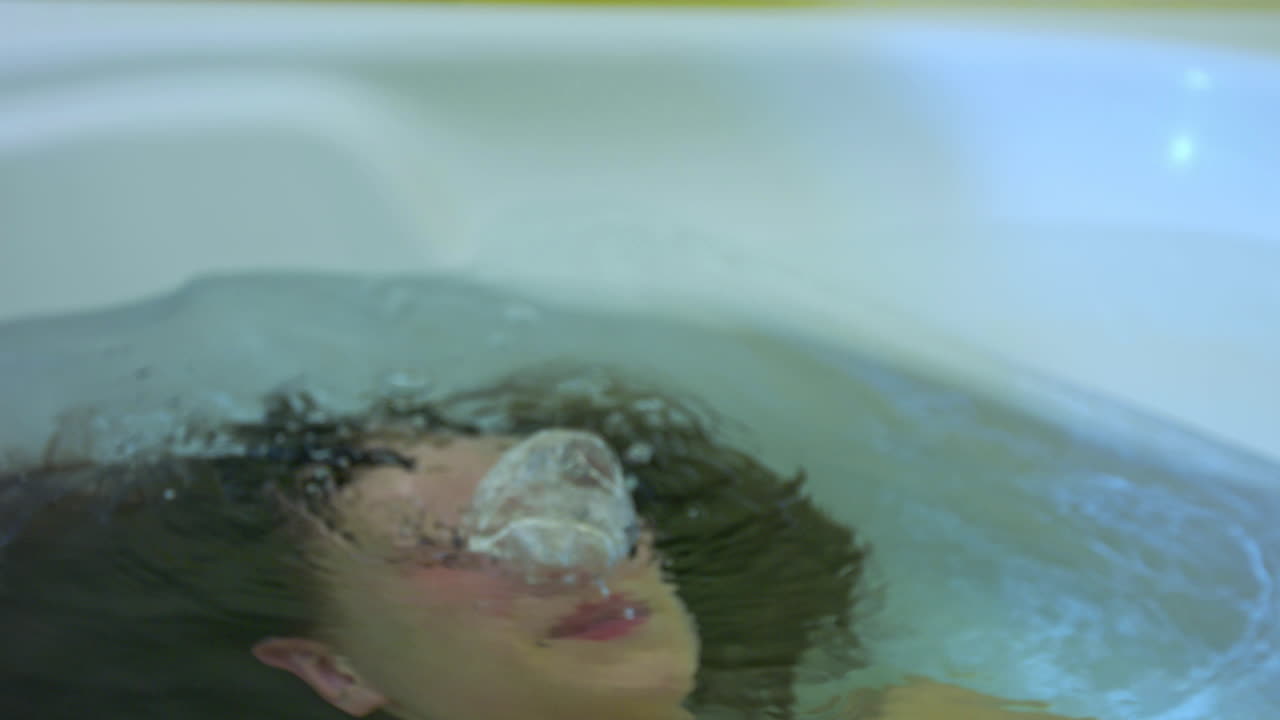 The young woman was submerged under water. I dive in the bathtub. Exhales. Oxygen bubbles escape from her nose. She is drowning. Danger in the bathtub