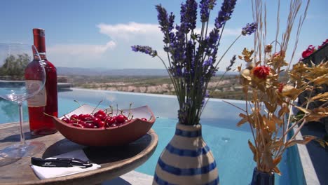 Tray-With-Red-Wine-and-Bowl-of-Cherries-Sitting-by-a-Pool-With-Beautiful-Turkish-Landscape-in-Background-on-a-Sunny-Day,-ultimate-luxury-life-in-a-cappadocia-cave-hotel