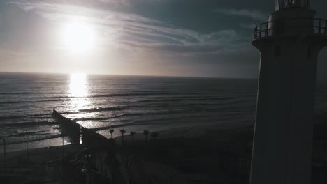 aerial shot of the lighthouse in tijuana beach with the wall of the border in the back