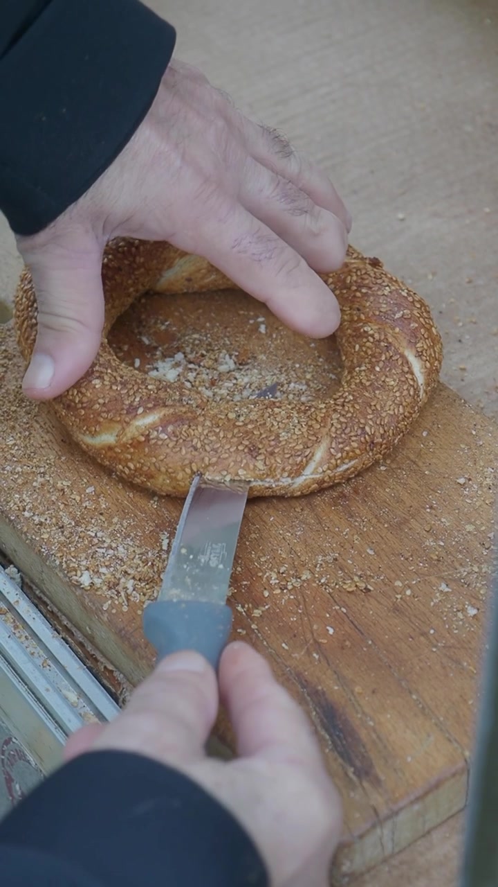 Man's Hands Slicing a Traditional Turkish Simit on a Wooden Board