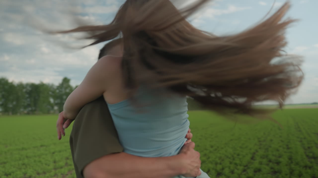 man lifting woman in arms after playful run across green field at sunset, she laughs and wraps arms around his shoulders as he turns with warm smile under pastel sky