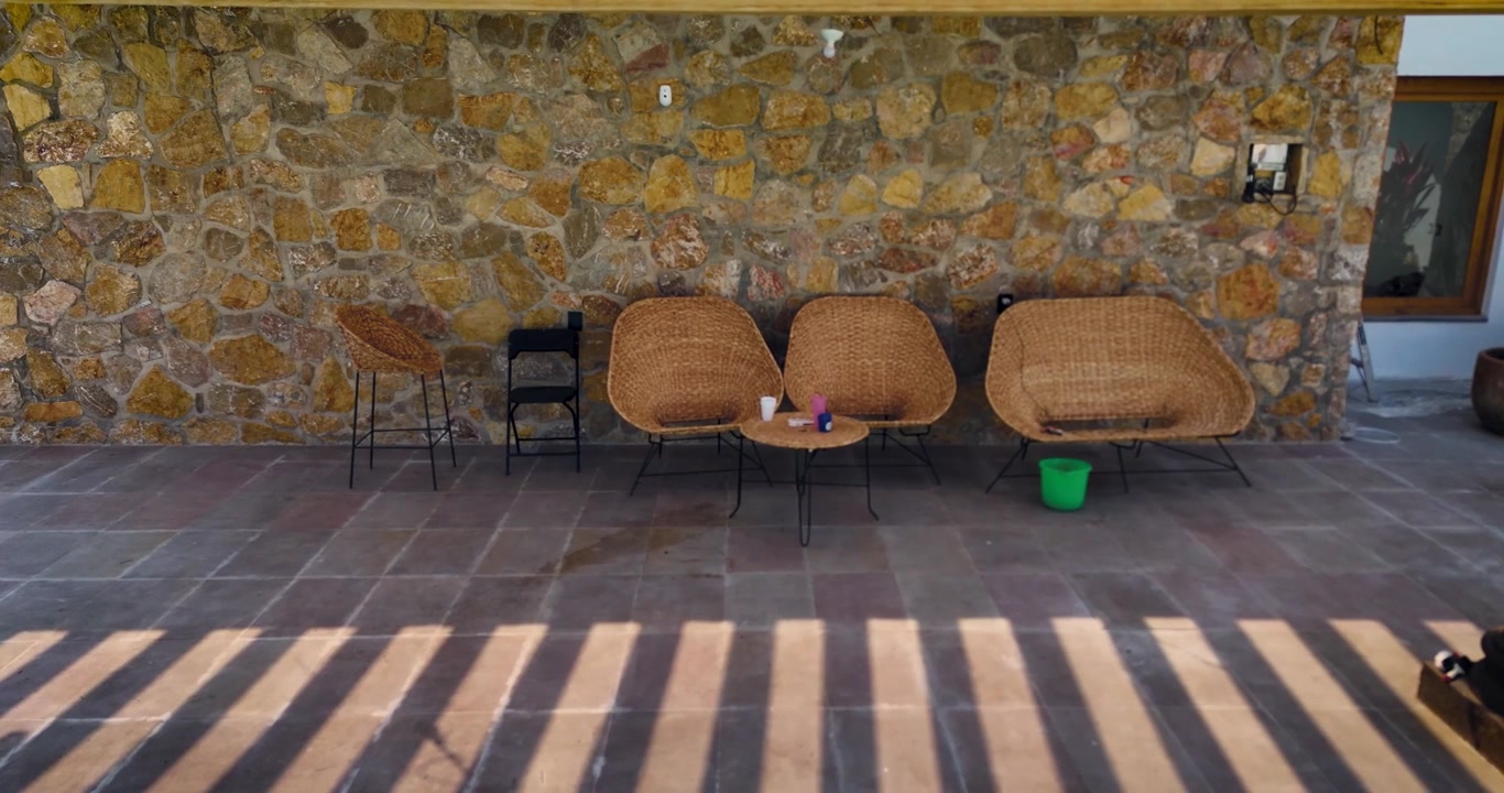 Panoramic shot of an outdoor seating area under a wooden pergola roof, finished with a stone wall in Mexico