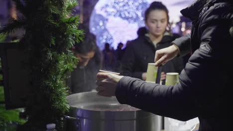 woman pouring mulled wine in a cup christmas lights in background. montpellier