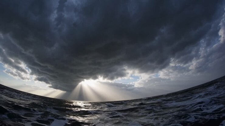 Ripresa video drammatica dal basso angolo di nuvole tempestose sopra un mare in tempesta, che cattura i raggi del sole che squarciano le nubi
