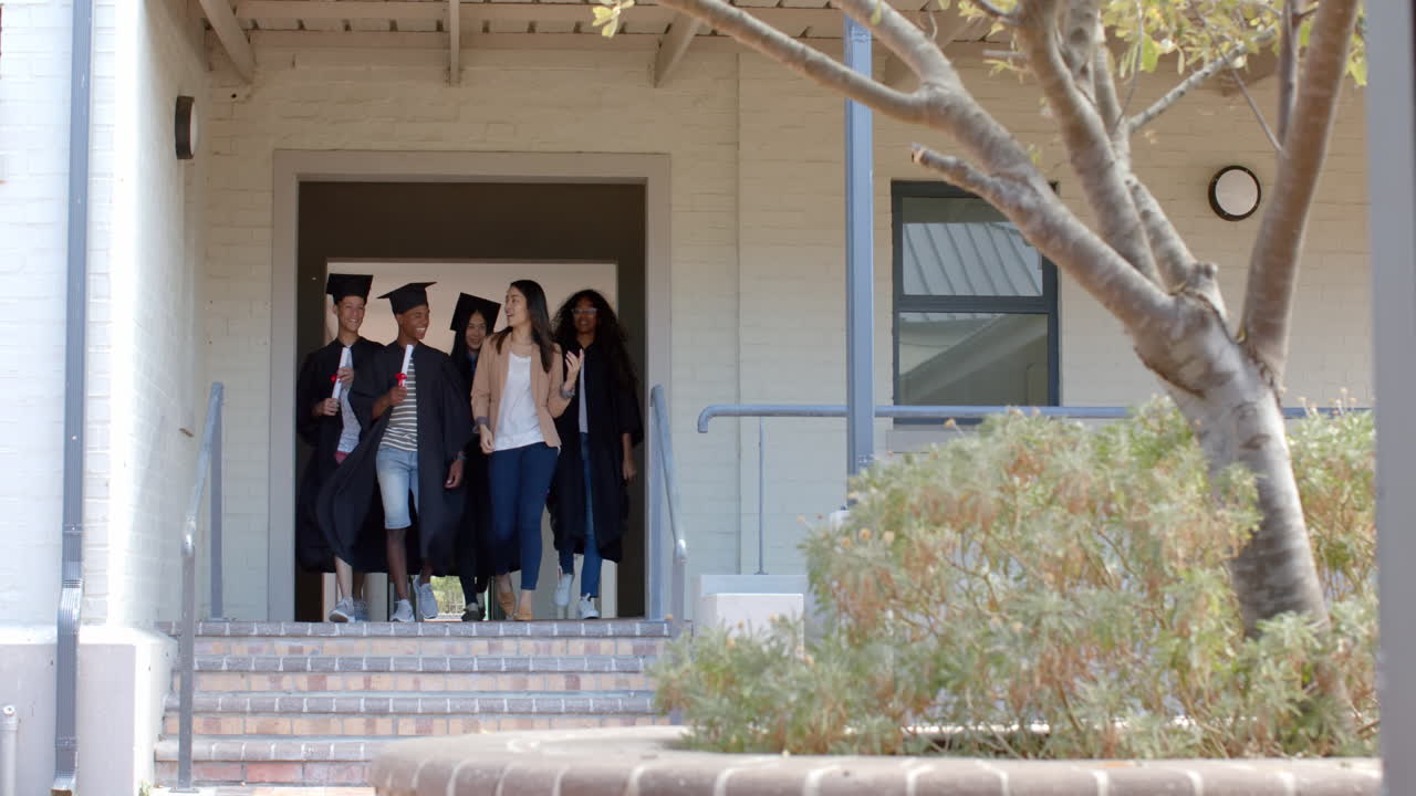 Diverse group of graduates steps out of a high school building