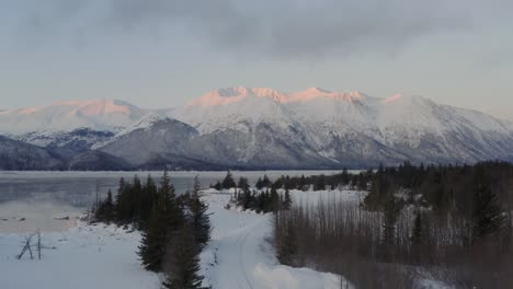 majestic alaskan mountains with last sunlight hitting edge, flyover pine trees, aerial forward