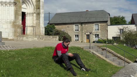 Motorcycle-woman-relaxing-on-the-grass-engrossed-in-looking-at-and-texting-on-a-mobile-phone,-drone-dolly-forward-at-low-angle