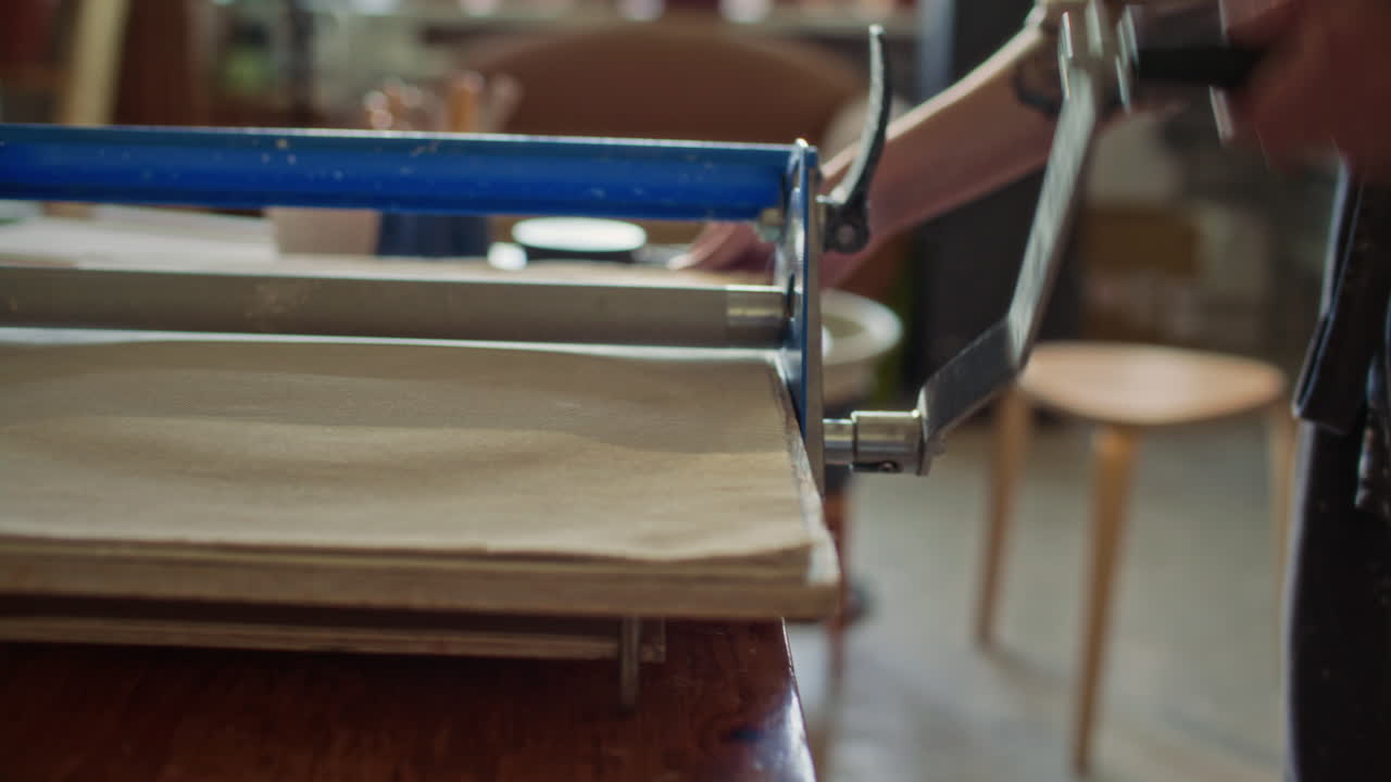 Close Up of Female Potter Turning Handle of Slab Roller while Flattening Clay