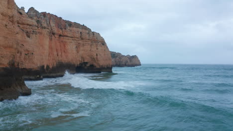 Pancarta-De-Fondo-Escénica-Vista-Aérea-De-Drones-De-La-Costa-De-Lagos-Con-Olas-Rompiendo-Contra-Los-Acantilados-En-Un-Día-Nublado,-Portugal