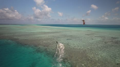 kitesurfista deslizándose sobre aguas tropicales azules claras con cometa en el cielo, disparo de seguimiento aéreo de drones