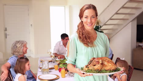 Madre-Feliz-Mostrando-Pavo-Asado-A-La-Cámara-Con-Su-Familia-Detrás-De-Ella