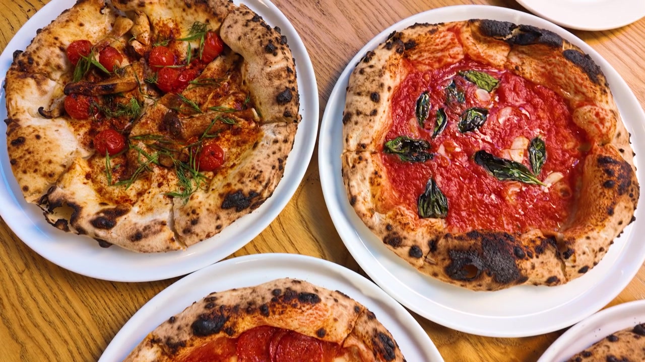 Una ripresa dall'alto mostra varie pizze gourmet servite su piatti bianchi in un ristorante.