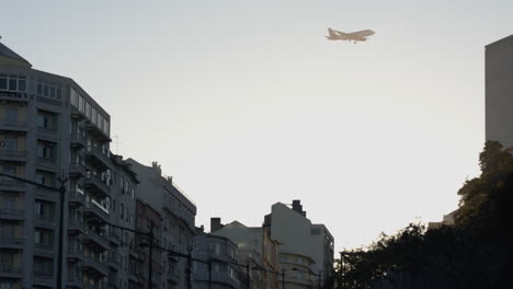 an airplane flying high in the sky over the buildings in marques de pombal roundabout in lisbon, portugal - low angle shot