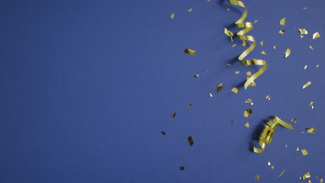 Video-of-gold-streamers-and-confetti-on-dark-blue-background,-with-copy-space