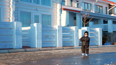 lovely little baby boy wearing warm clothes and sunglasses runs outdoors. cute toddler at the alley along the cottages.
