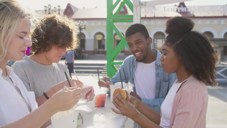 group of cheerful multiethnic friends eating street food in the city while chatting and spending time together