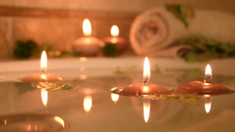 relaxing spa background with candles floating in the bath water, some green petals and a towel near the water surface