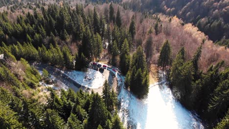 Aerial,-tilt-down,-drone-shot,-of-a-car-on-a-winding,-hillside-road,-in-Romanian-forest,-on-a-mountain,-on-a-sunny,-fall-day,-in-Romania