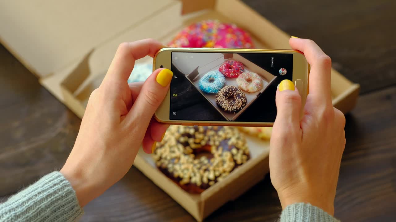 las manos de la mujer toman fotos con el teléfono inteligente de deliciosas rosquillas en la caja