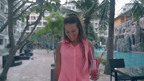 girl carries cocktail walks smiling near swimming pool