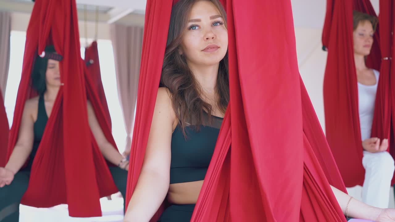 женщины сидят в гамаках для йоги и практикуют медитацию