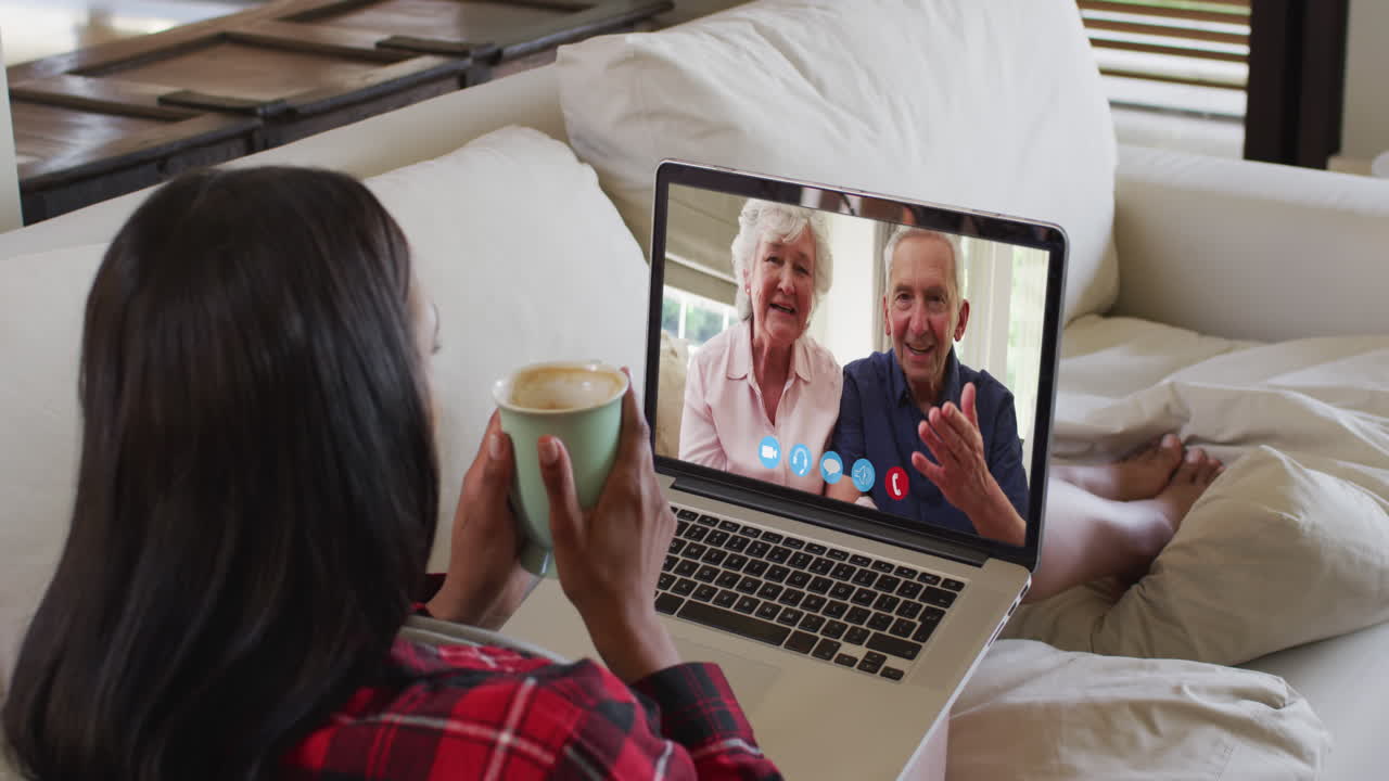 mujer biracial en chat de video portátil tomando café durante la navidad en casa