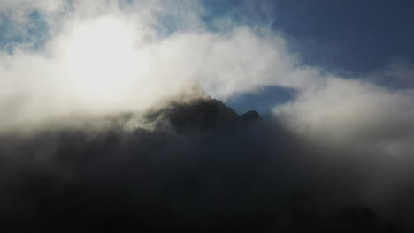 cinematic drone shot of clouds on top of mountain peaks with the sun casting shadows in the clouds