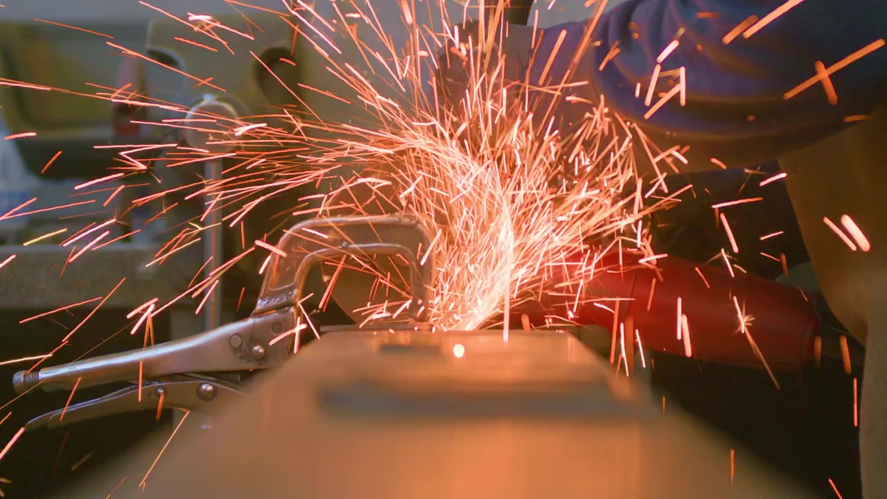 Angle grinder sparks table level low angle view, static close up shot. Fiery shower shooting towards camera resting on workbench during metal fabrication.