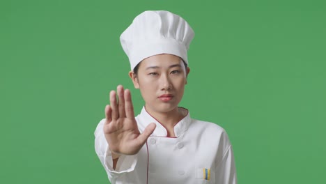 close up of asian woman chef looking at camera and disapproving with no hand sign in the green screen background studio