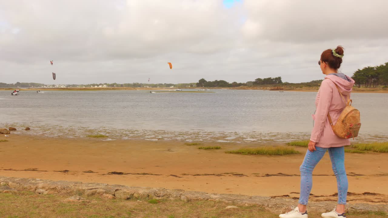 Woman by beach in Brittany, France with kite surfers in background