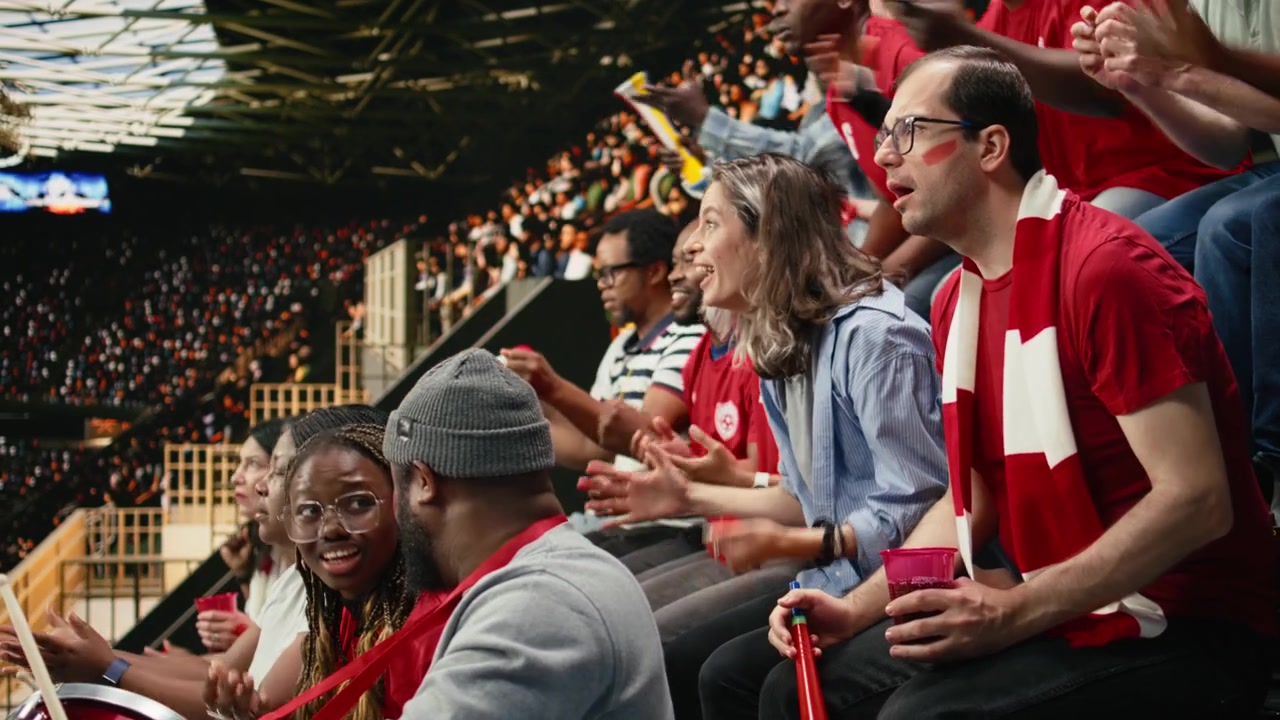 Aficionados de fútbol de rojo viendo un intenso partido de fútbol en vivo desde un estadio abarrotado.