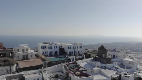 High-atop-Santorini,-aerial-flies-toward-round-stone-Windmill-Villa