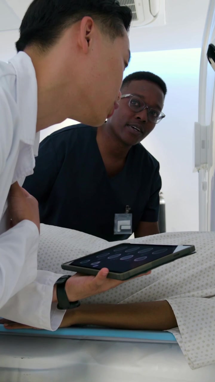 Vertical video: Reviewing tablet prompt, whitecoat MD and tech aligning patient for scan on gantry
