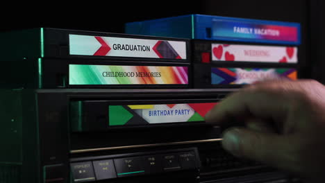inserting birthday party vhs video cassette tape into vcr and pressing play button, close up