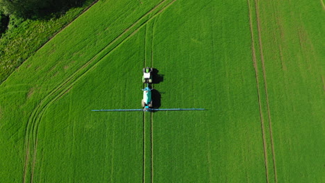 farmer in tractor spraying fertilizer on green field