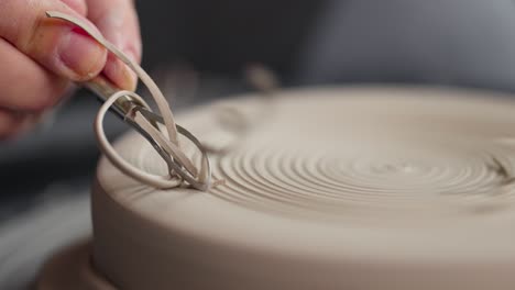 close-up of woman's hands which shaping workpiece with a tool in a pottery studio. clay shavings. slow motion