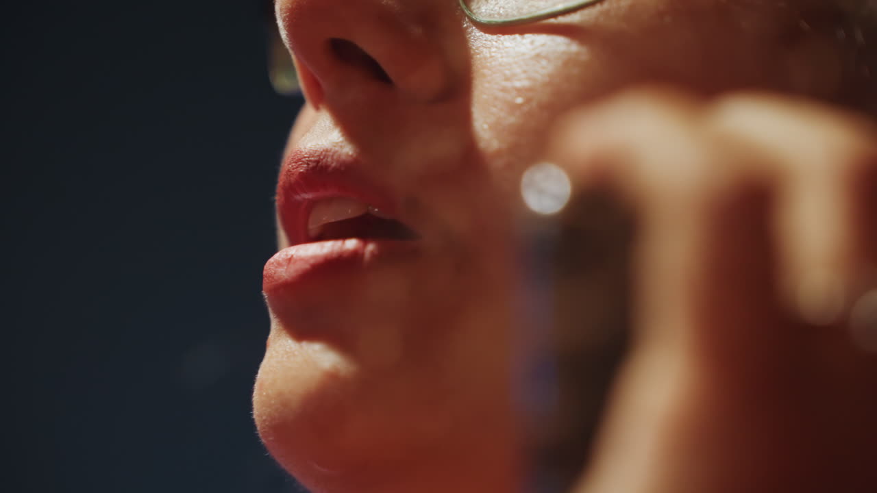 Lippen aus niedriger Perspektive nah am Mikrofon, eng sprechend, intensive Probe oder Aufnahmesession mit Brille, die warmes Bühnenlicht einfängt, sichtbarer Schweiß und Hauttextur, Hand hält kleines Mikrofon