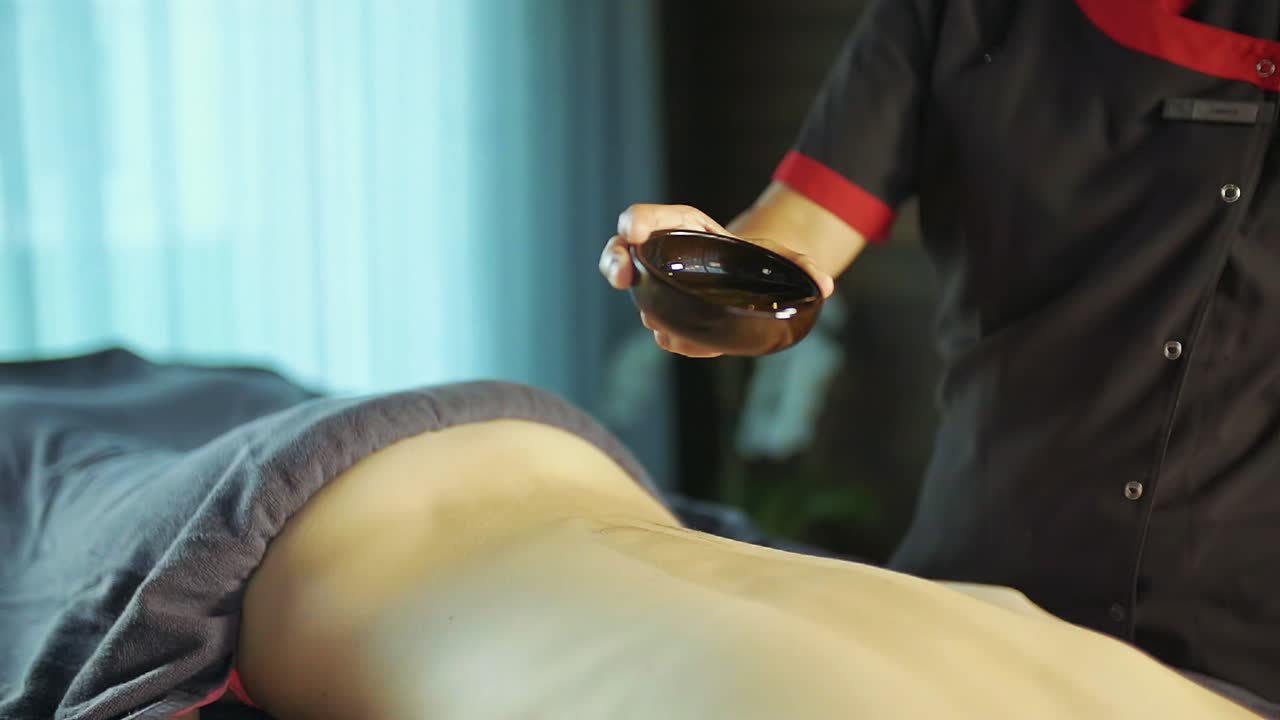 masseuse pours massage oil on woman's back. slow motion